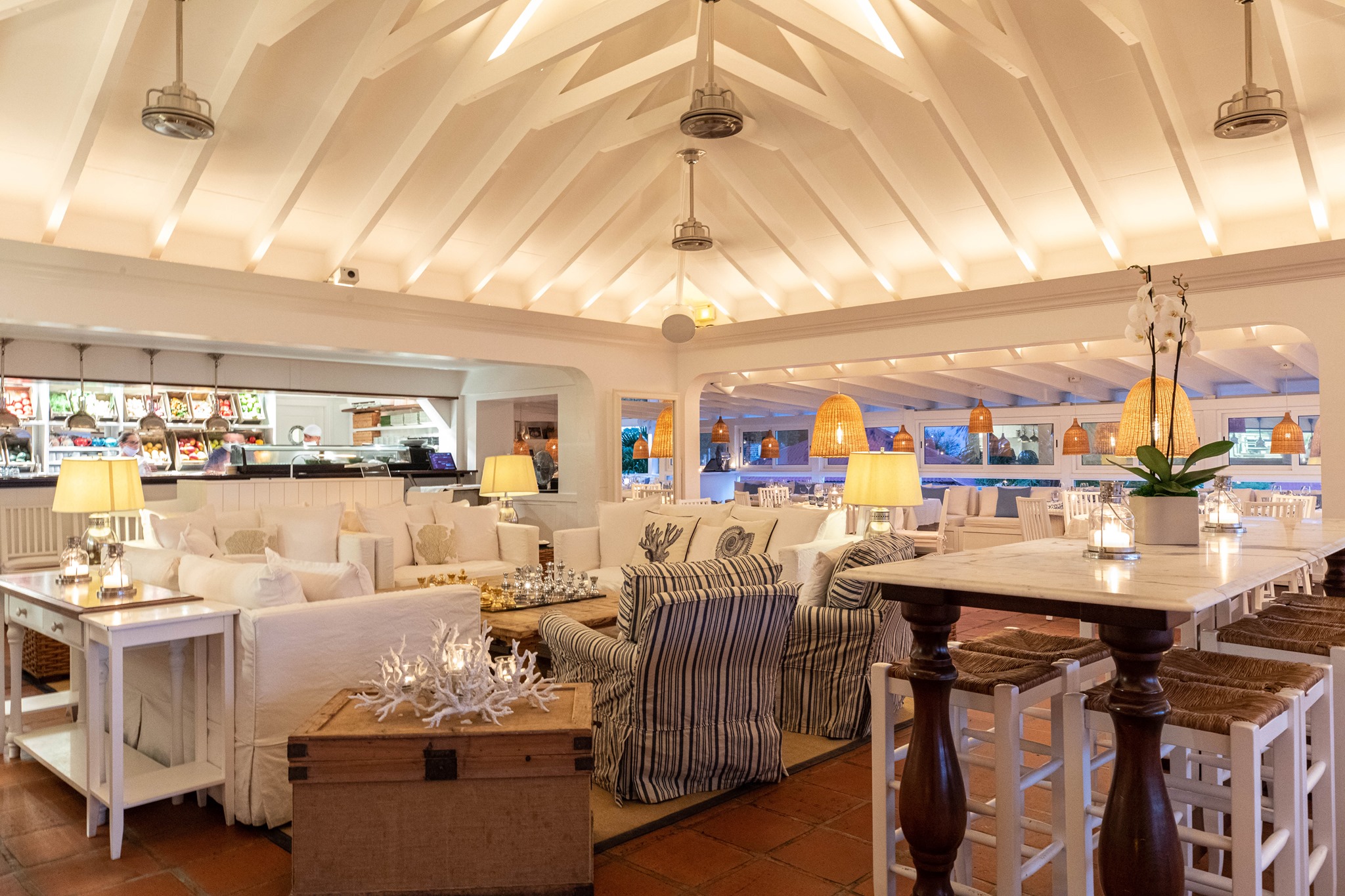 The Bonito dining room — white slipcovered sofas, raffia pendants, marble high-tops, candlelight